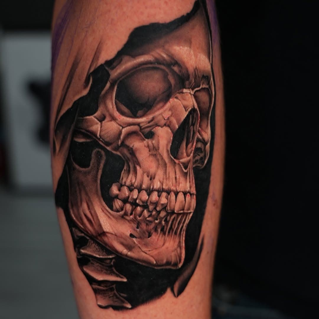 Black and grey realistic skull ripping through skin tattoo on leg by Ink Theory