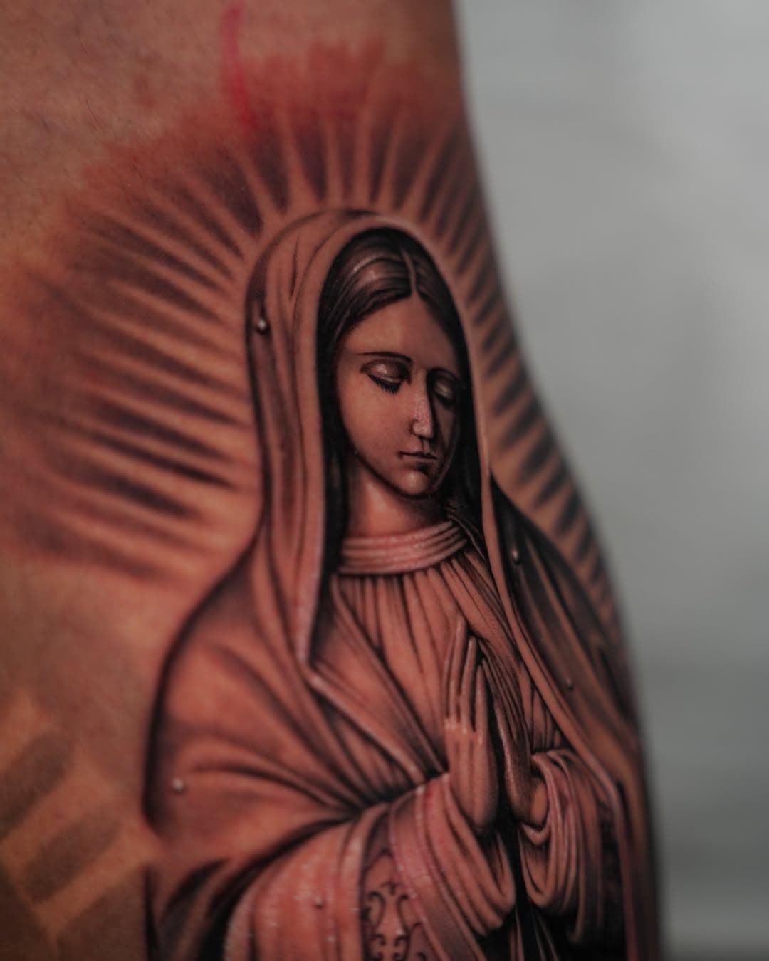 Black and grey Virgin Mary closeup portrait tattoo with radiant halo by Ink Theory