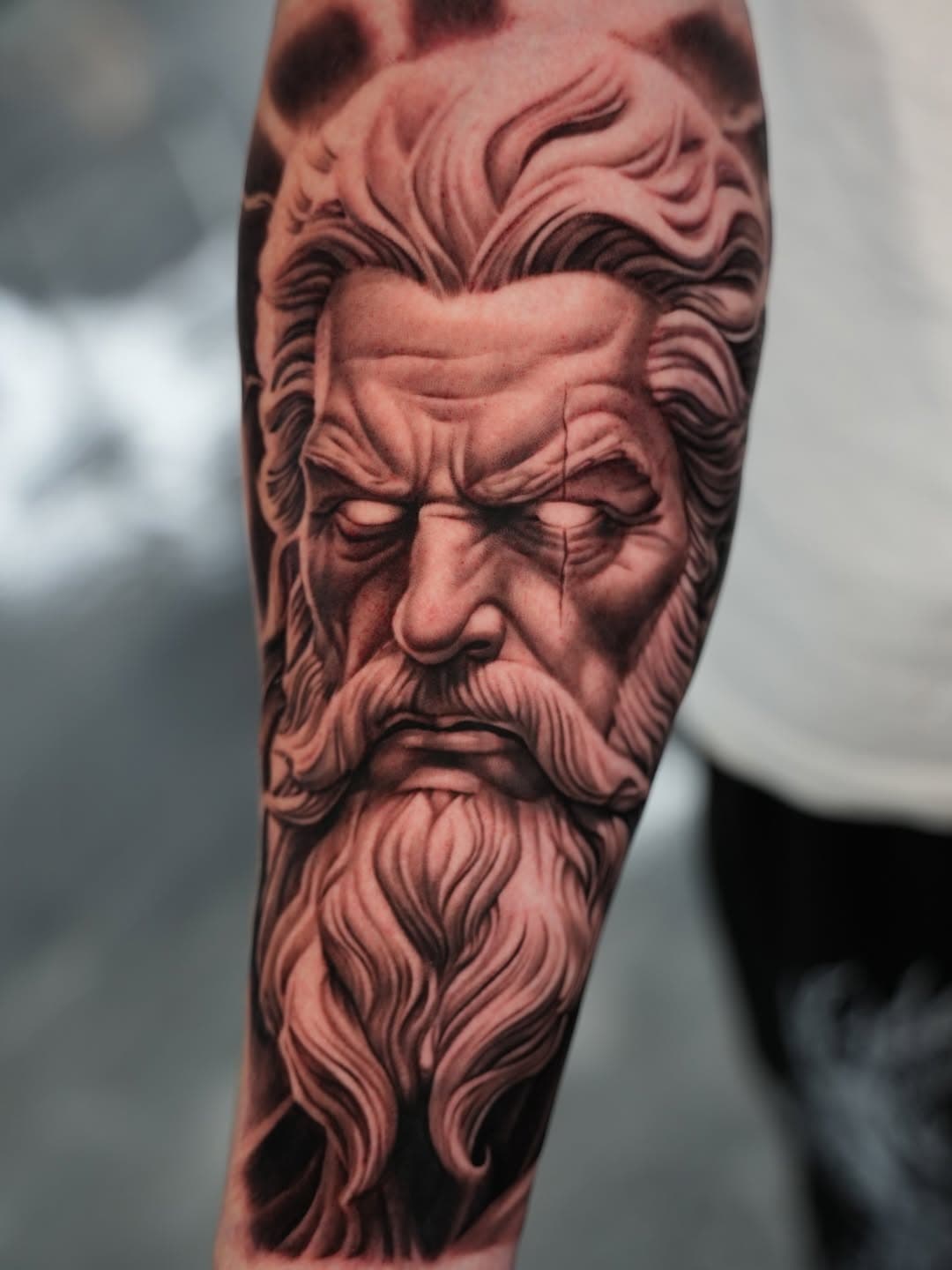 Black and grey realistic Greek god bearded portrait tattoo on forearm by Ink Theory