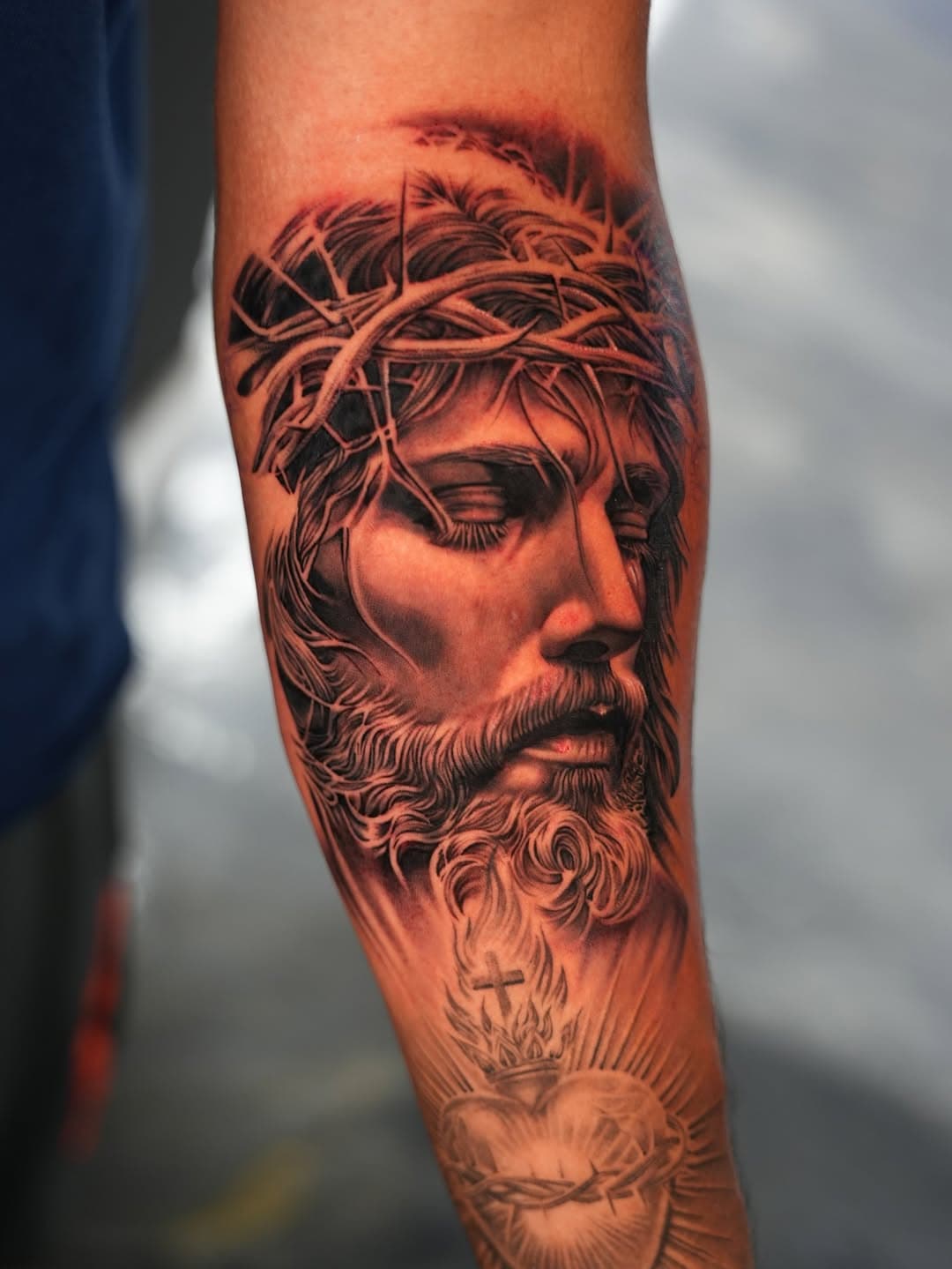 Black and grey Jesus Christ with crown of thorns and sacred heart tattoo on forearm by Ink Theory