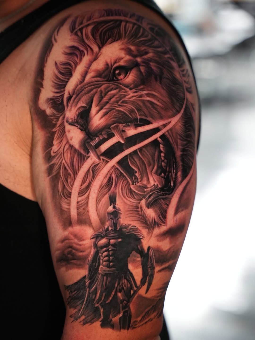 Black and grey roaring lion and Spartan warrior tattoo on upper arm by Ink Theory
